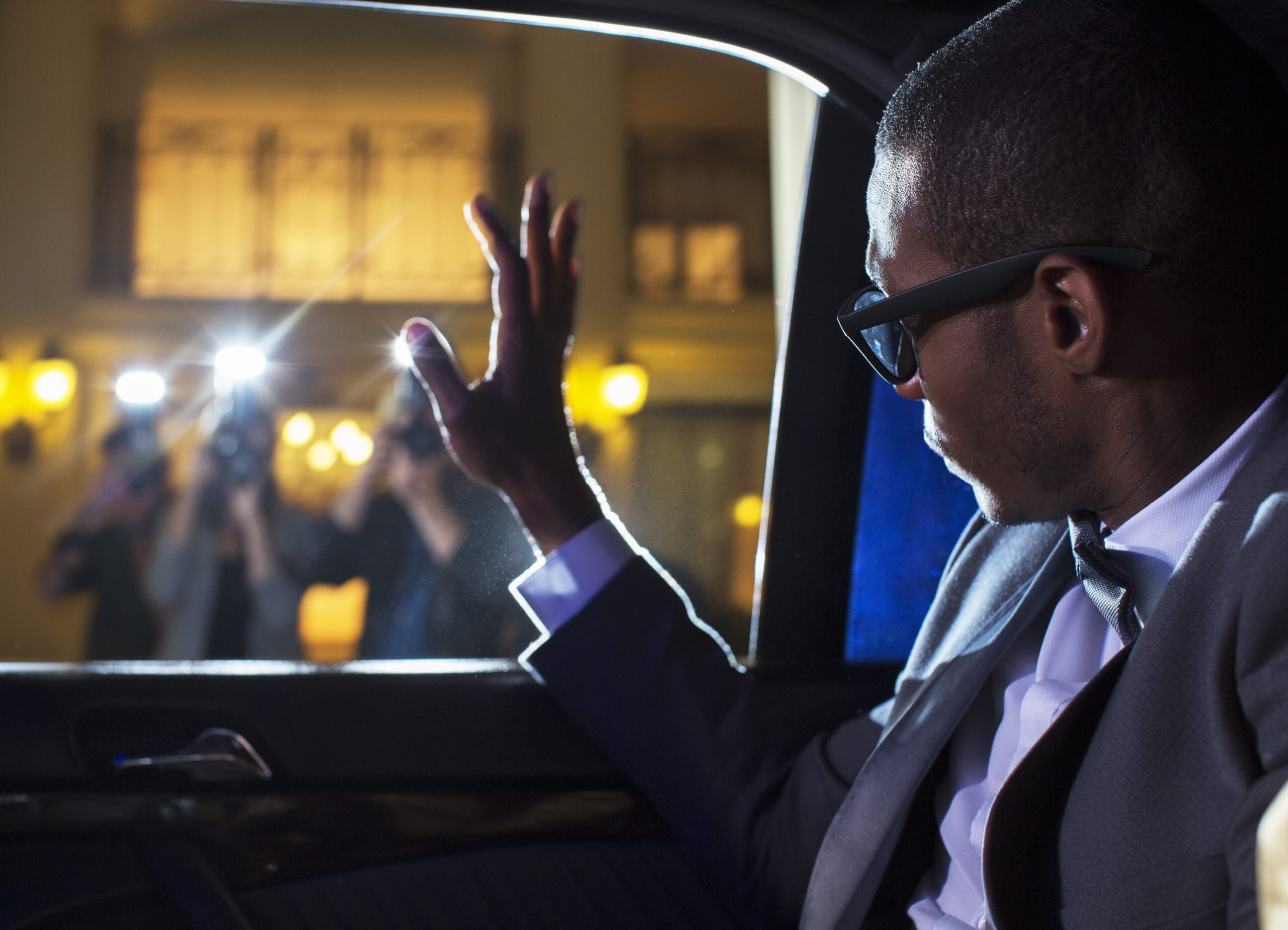 Celebrity in limousine waving at paparazzi photographers